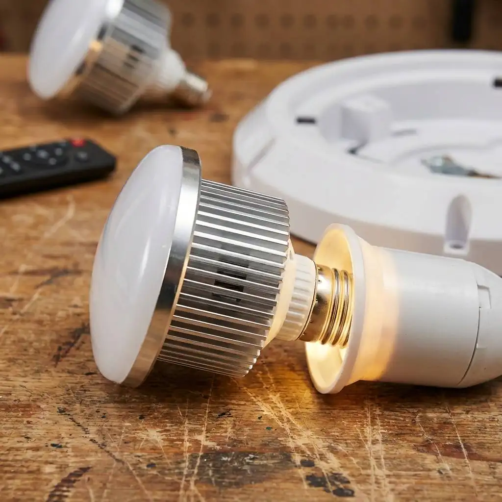 Close-up of a light bulb being screwed into a socket on a wooden workbench with plastic housing in the background. Close-up of a light bulb being screwed into a socket on a wooden workbench with plastic housing in the background.